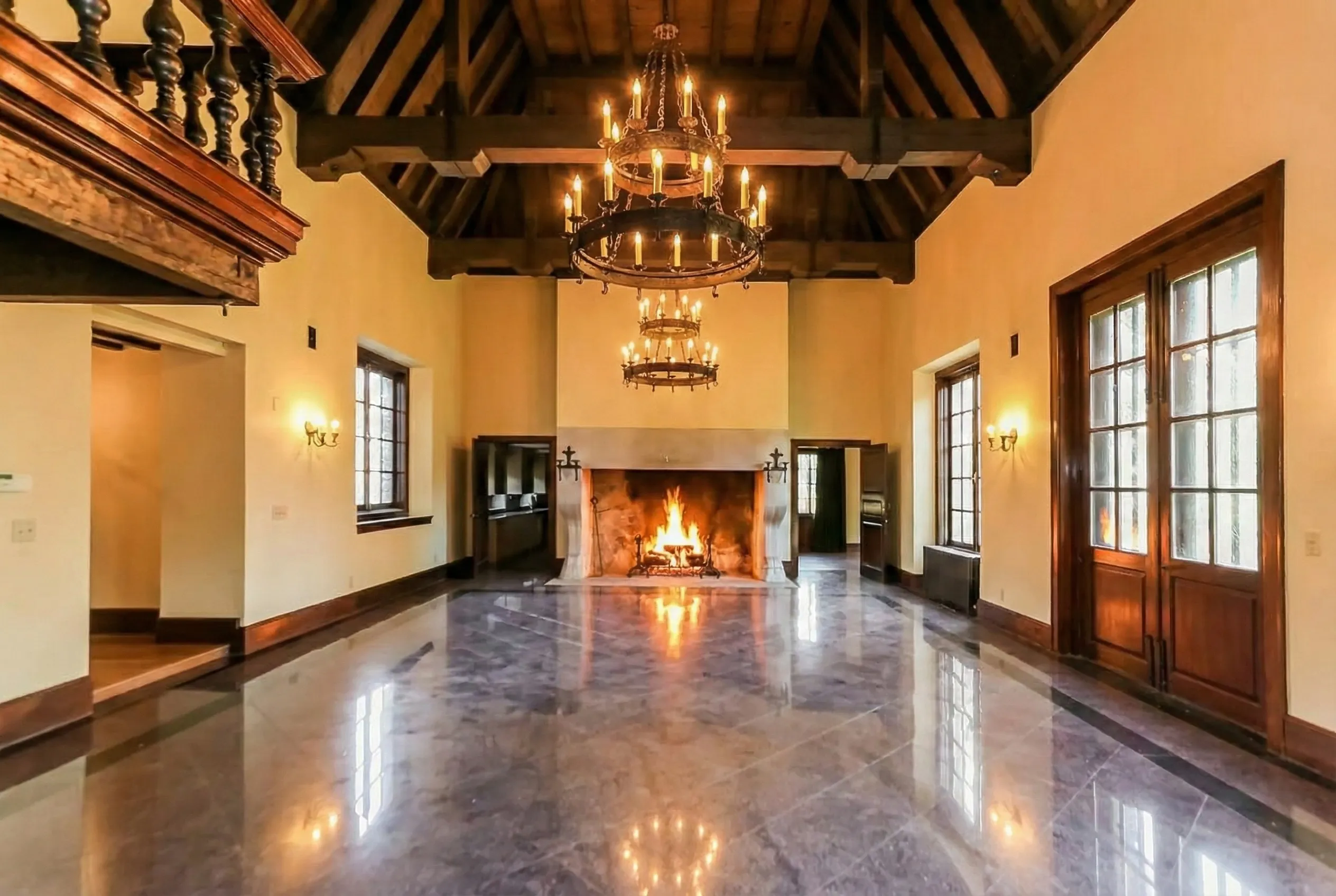 The Great Hall — marble floors, exposed timber ceiling, iron chandeliers, and a roaring fireplace